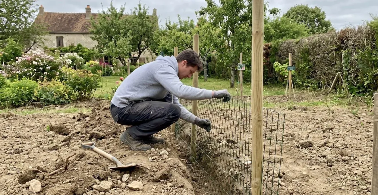 Personne vue de dos installant un grillage dans une tranchée creusée dans un jardin résidentiel français
